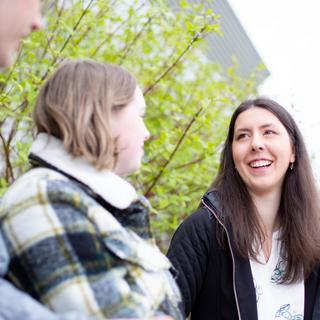 A young woman with long dark hair laghing with friends.