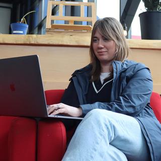 Young woman sitting on a red couch looking at a laptop