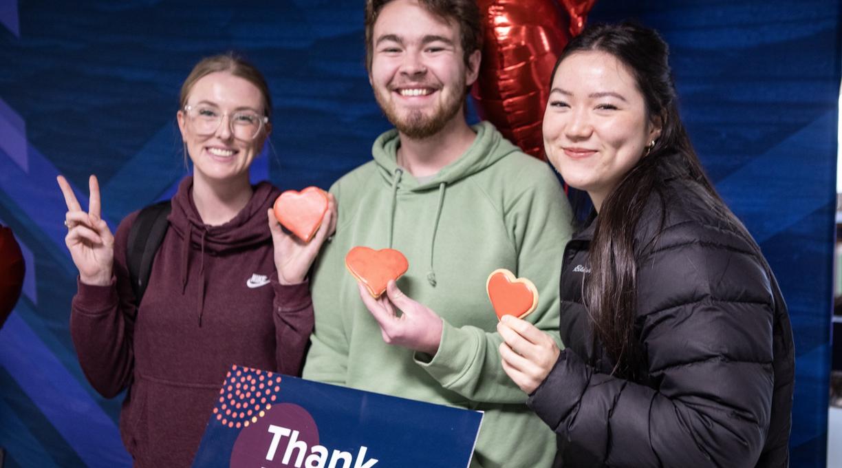 three students holding red heart cookies and a thank you sign