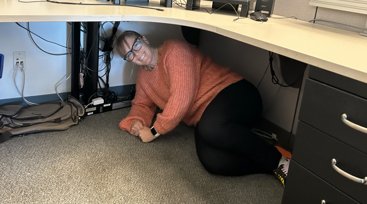 A VIU employee sheltering under a desk and smiling at the camera.