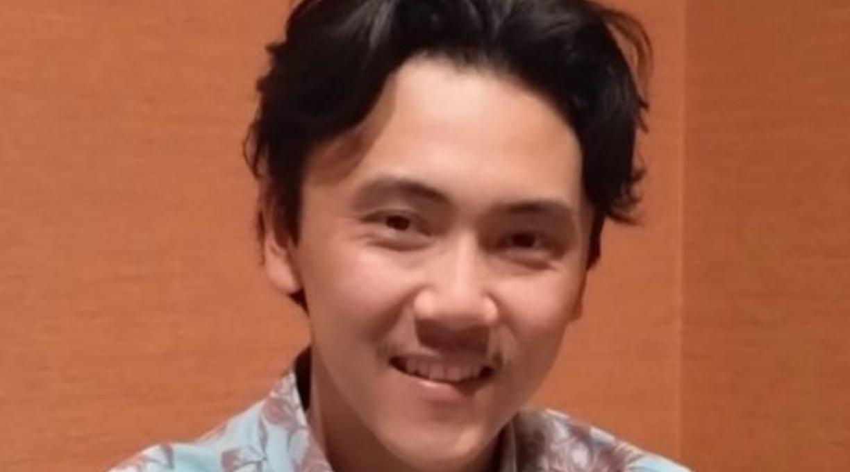 Kenji Boyko smiling. He wears a blue shirt decorated with maroon flowers.