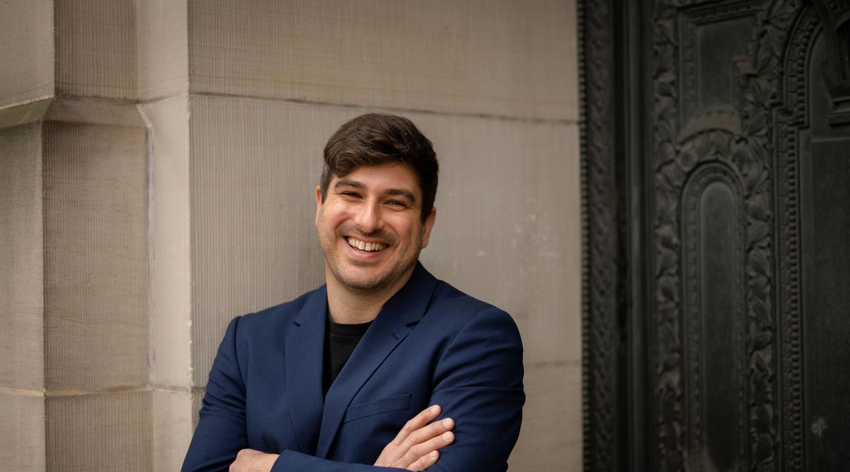 Michael MacKenzie standing against a wall and smiling at the camera.