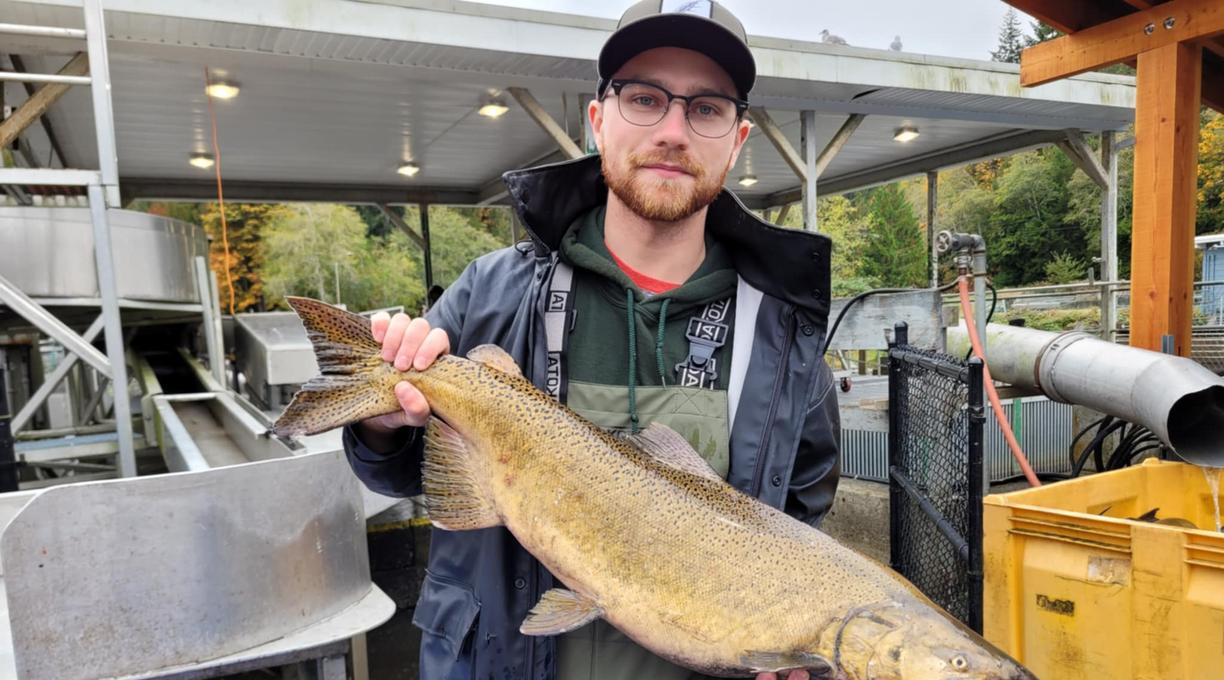 A man wearing hip waders and waterproof jacket holds a salmon