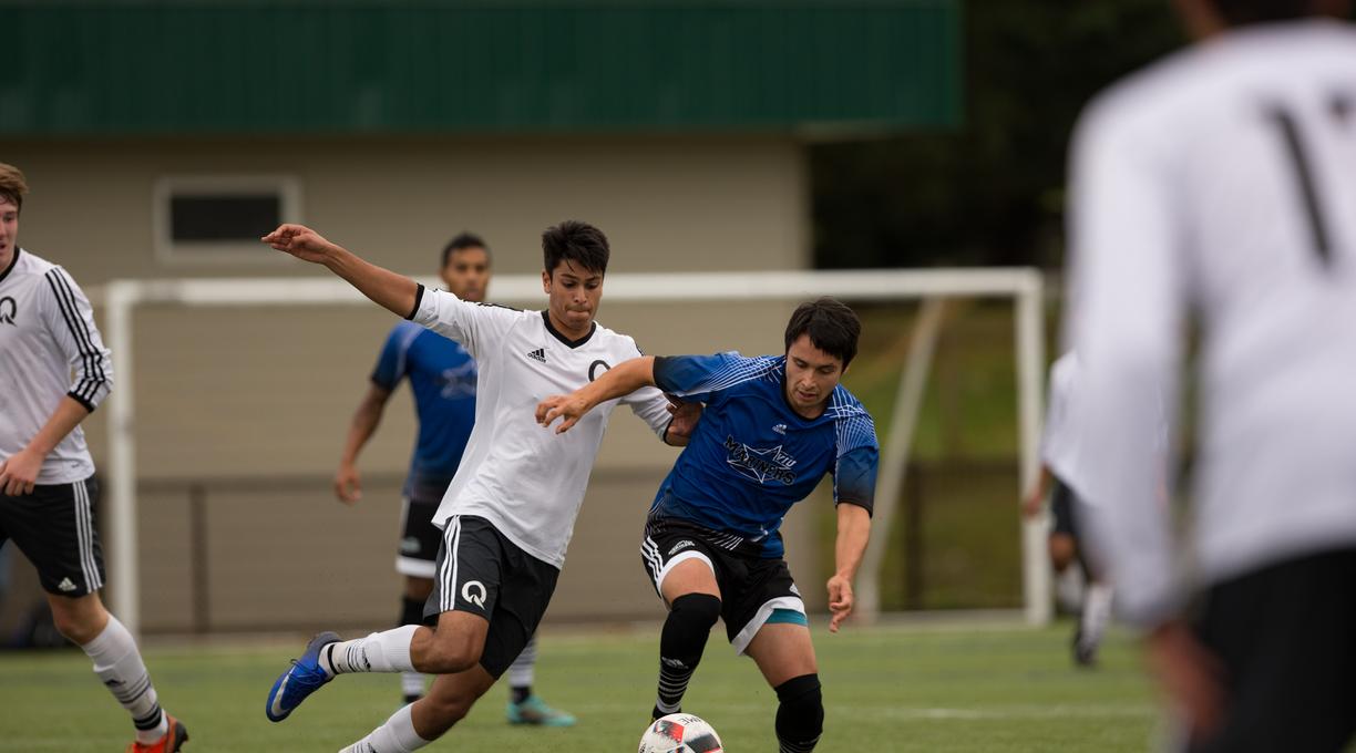 Mateo in the blue shirt runs down a soccer field with the ball pursued by an opposing player