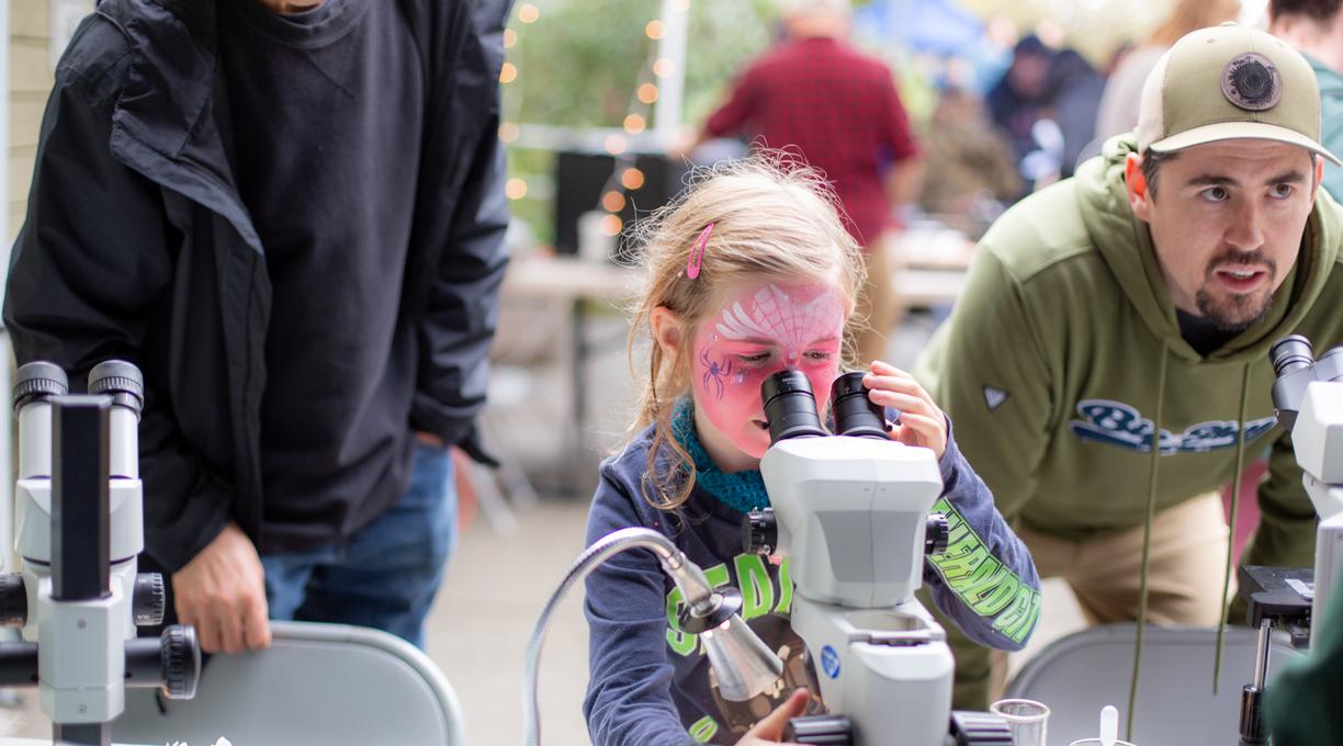 A young girl looking through a microscope during an exhibit at VIU Fest.