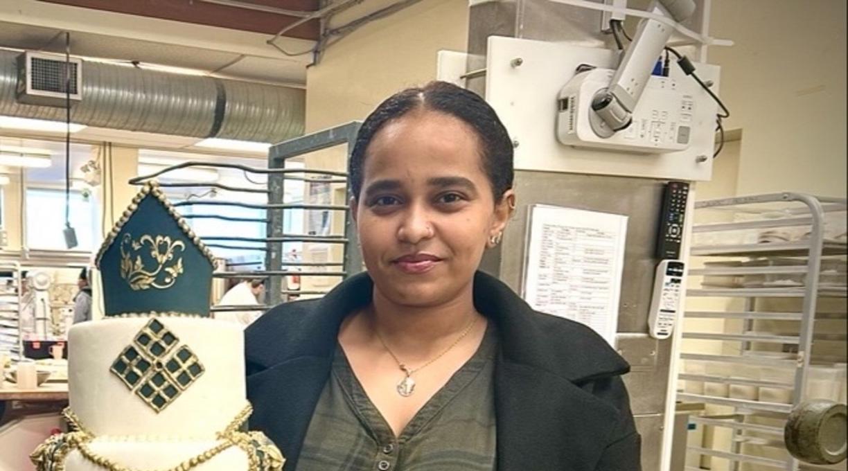 Zuhur Debasay holding a cake she made at VIU and smiling at the camera.