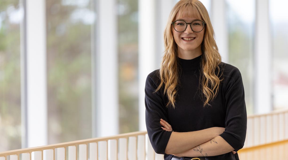 A student stands in front of a railing with her arms crossed