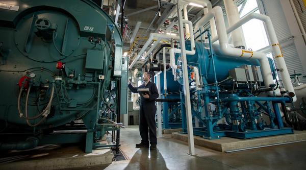 a power engineer inspects large tanks in a big machine room with sunlight peeking through the window