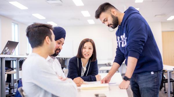 Four students look at a textbook together around a table