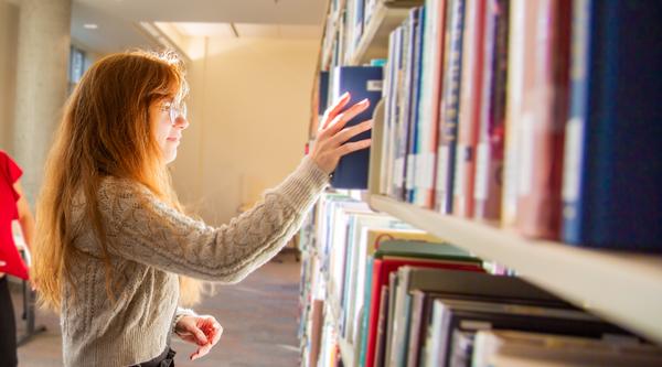 A student puts a book back on a library shelf