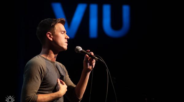 A student sings into a microphone with the VIU logo behind him