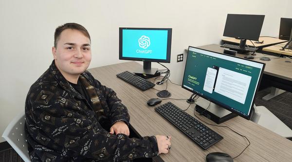 Andrew Szilagyi sitting in front of a computer and smiling at the camera. ChatGPT is on the screen in the background.