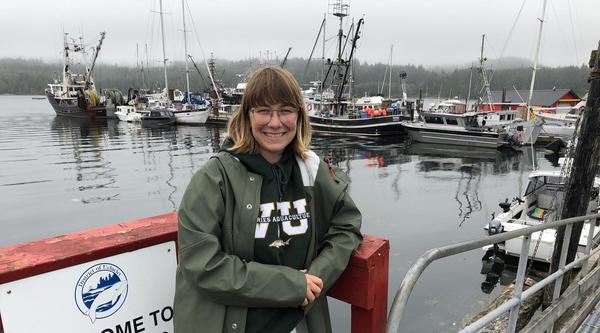 Allie Unger leans against a railing at Ucluelet harbour with boats anchored in the background.