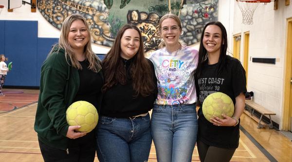 Four students in a gym holding volleyballs