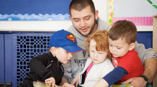 An early childhood educator reading a book to three kids