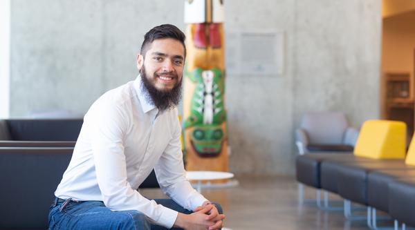 Fernando sits near the totem inside the Centre for Health and Science, VIU's Nanaimo campus