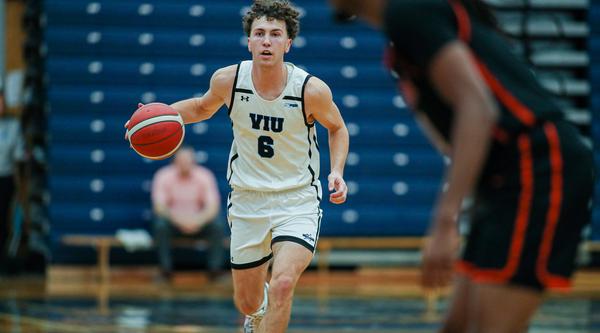 Ryan Bastian wearing a Mariners uniform running with the basketball during a game in a gym.
