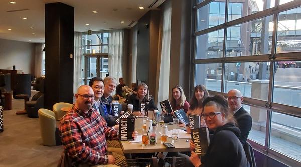 A group of people sit at a table, all holding copies of the same book