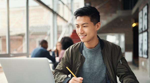 Student looks at a laptop screen and takes notes