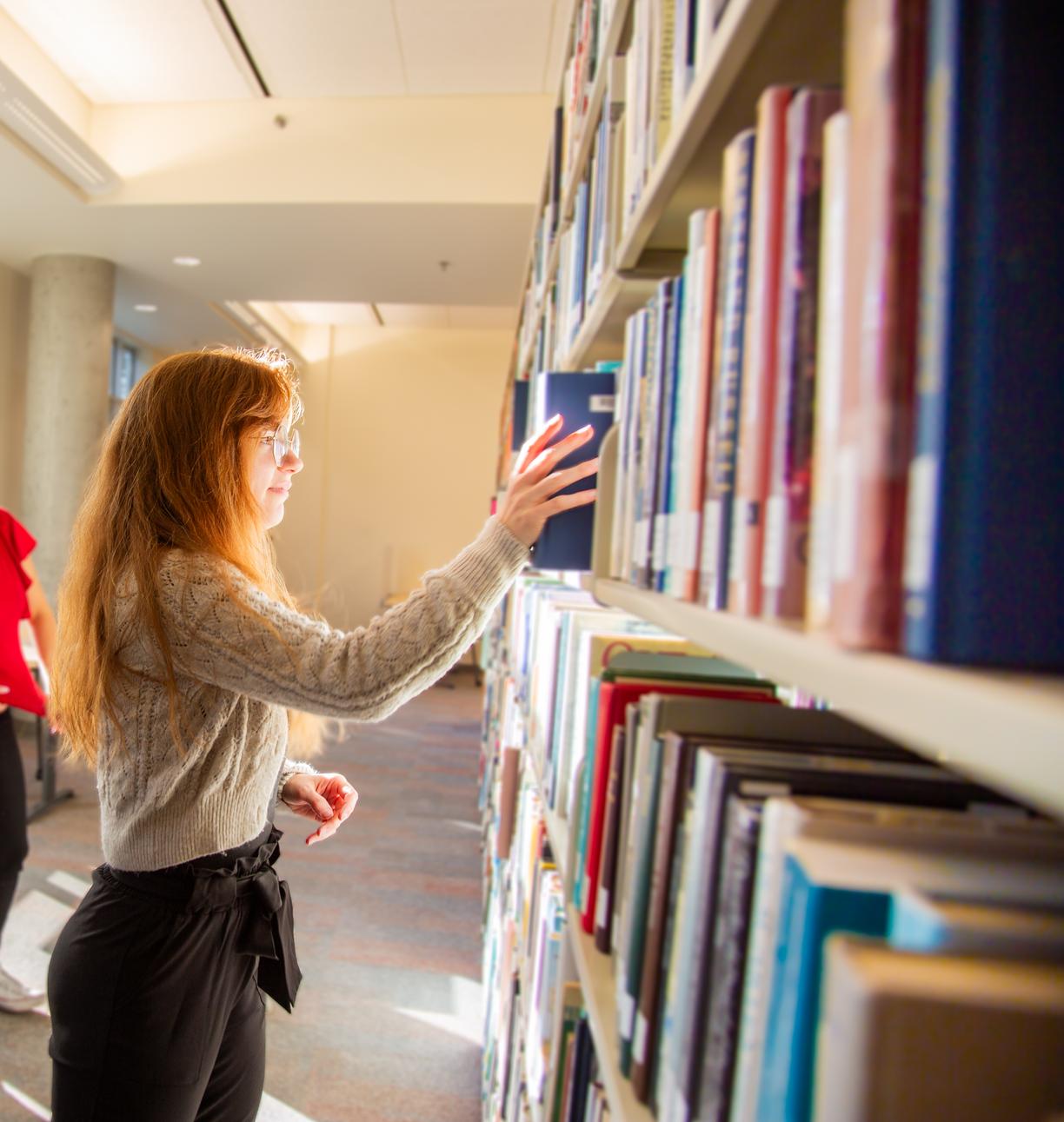 A student puts a book back on a library shelf