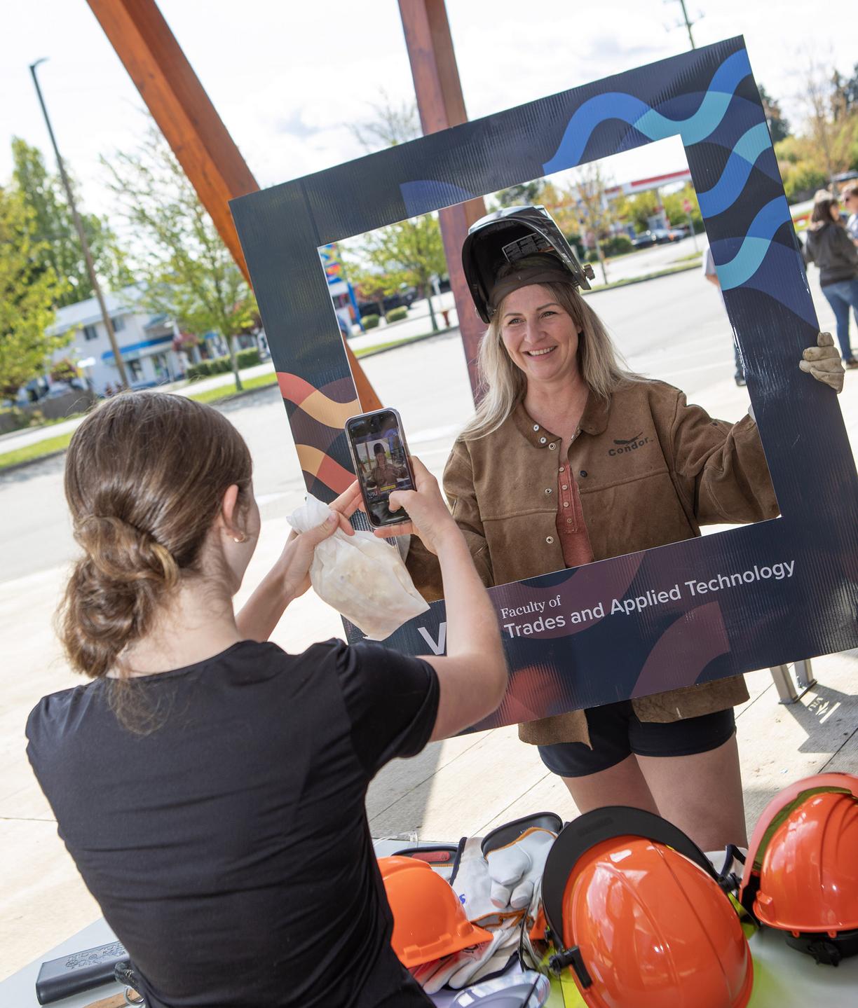 A student poses in a frame while another takes their photo