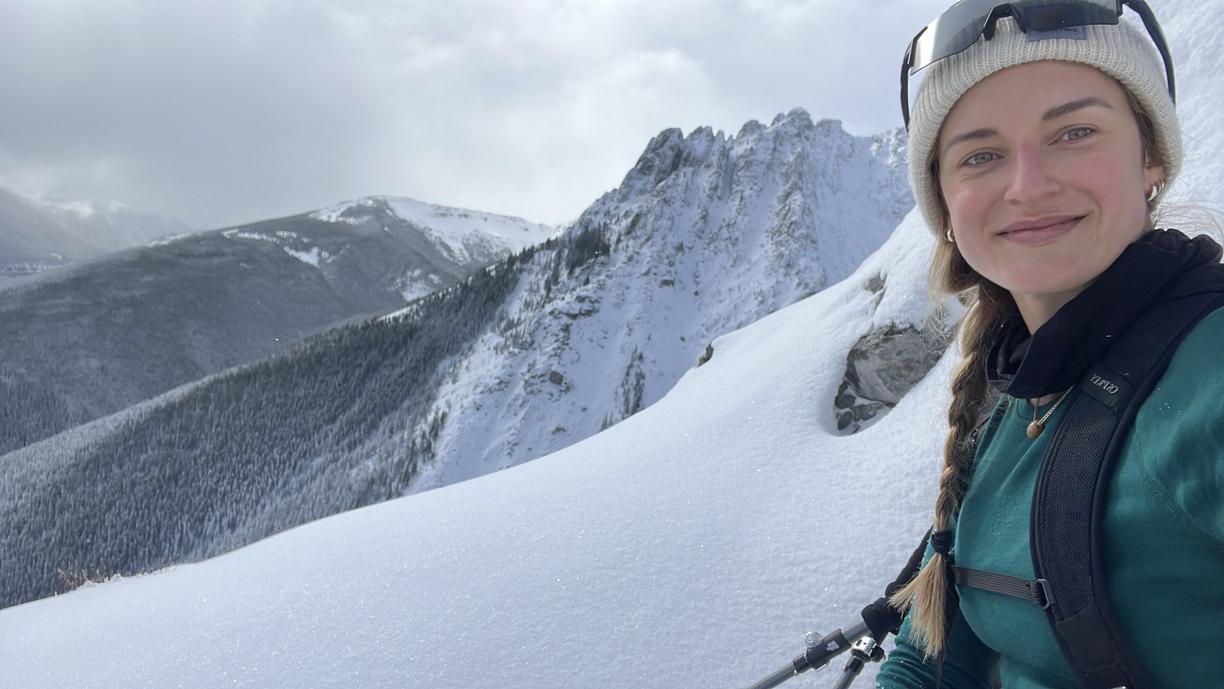 Andrea wearing ski gear smiles with a snowy mountainscape behind her