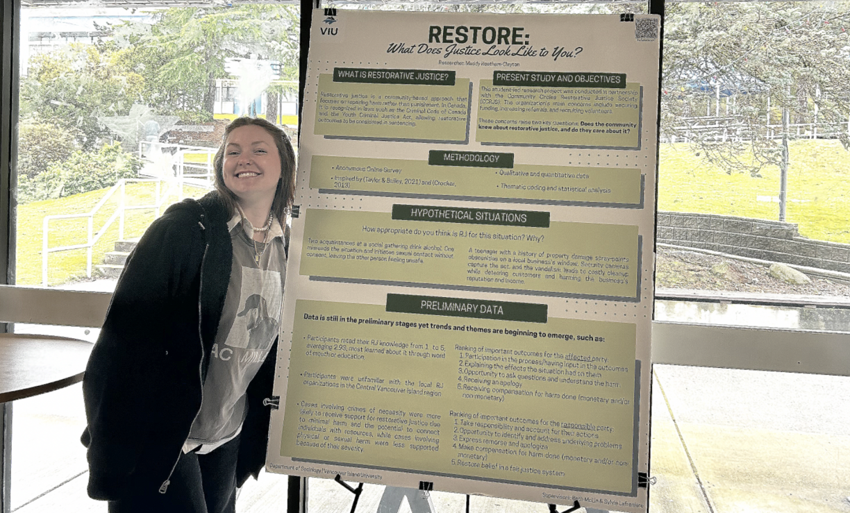 Madelyn Reetham-Clayton  standing beside her research poster and smiling.