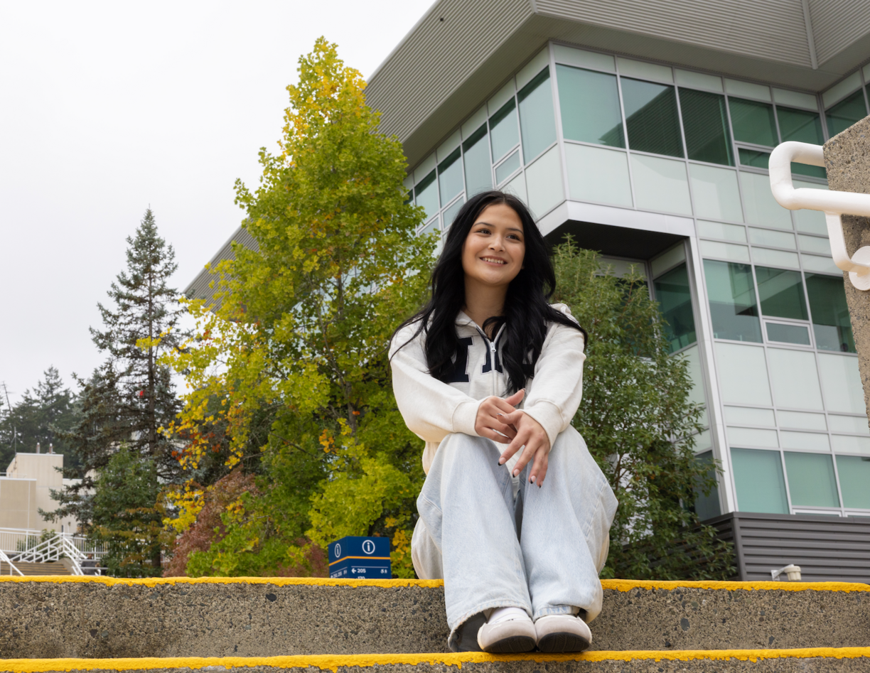 Marissa Tom-Charlie sitting on steps outside on a cloudy day, smiling and looking off into the distance
