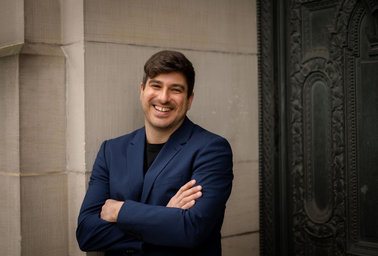 Michael MacKenzie standing against a wall and smiling at the camera.