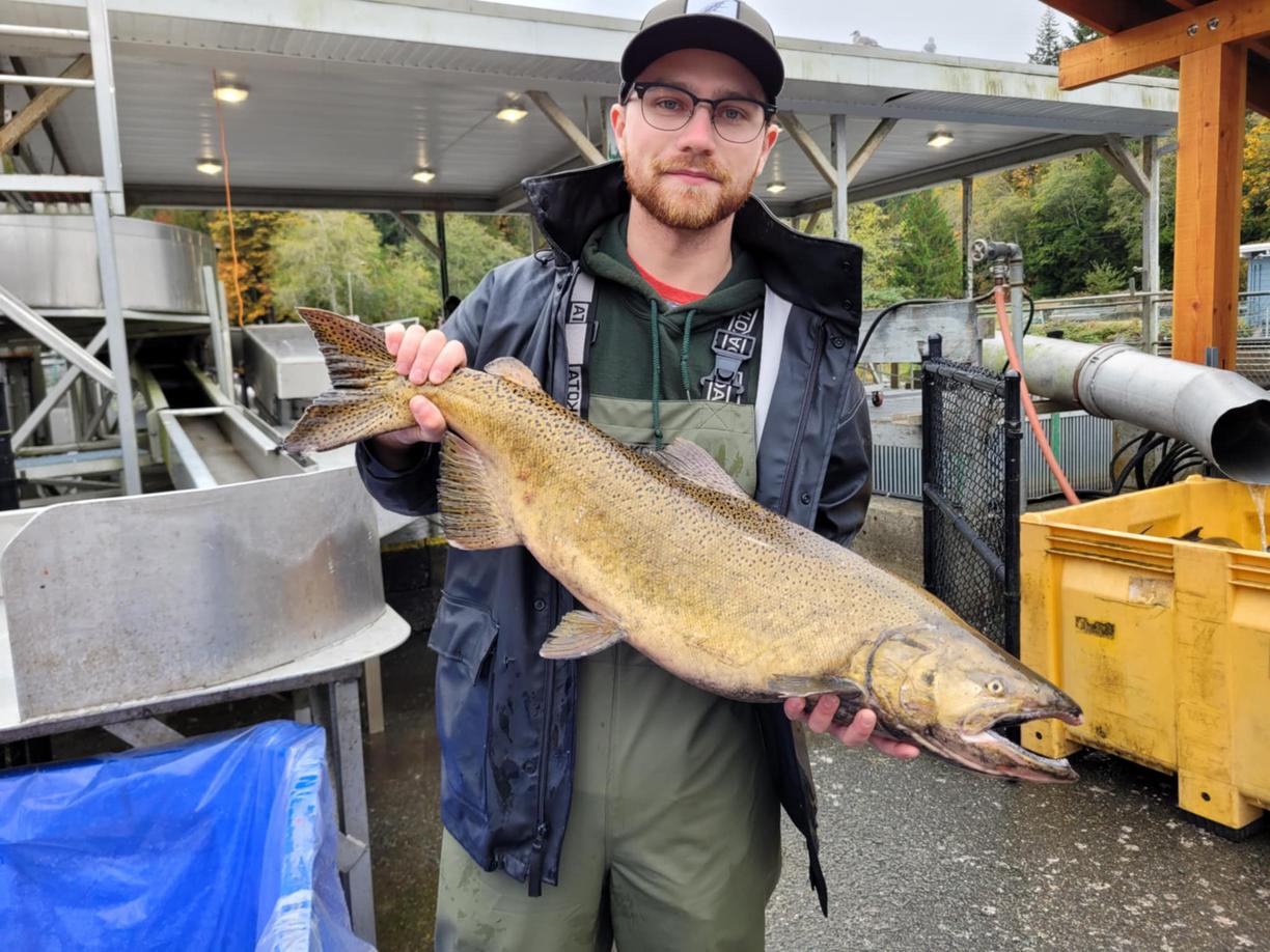 A man wearing hip waders and waterproof jacket holds a salmon