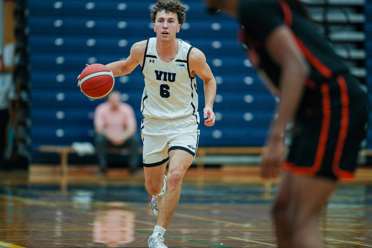 Ryan Bastian wearing a Mariners uniform running with the basketball during a game in a gym.