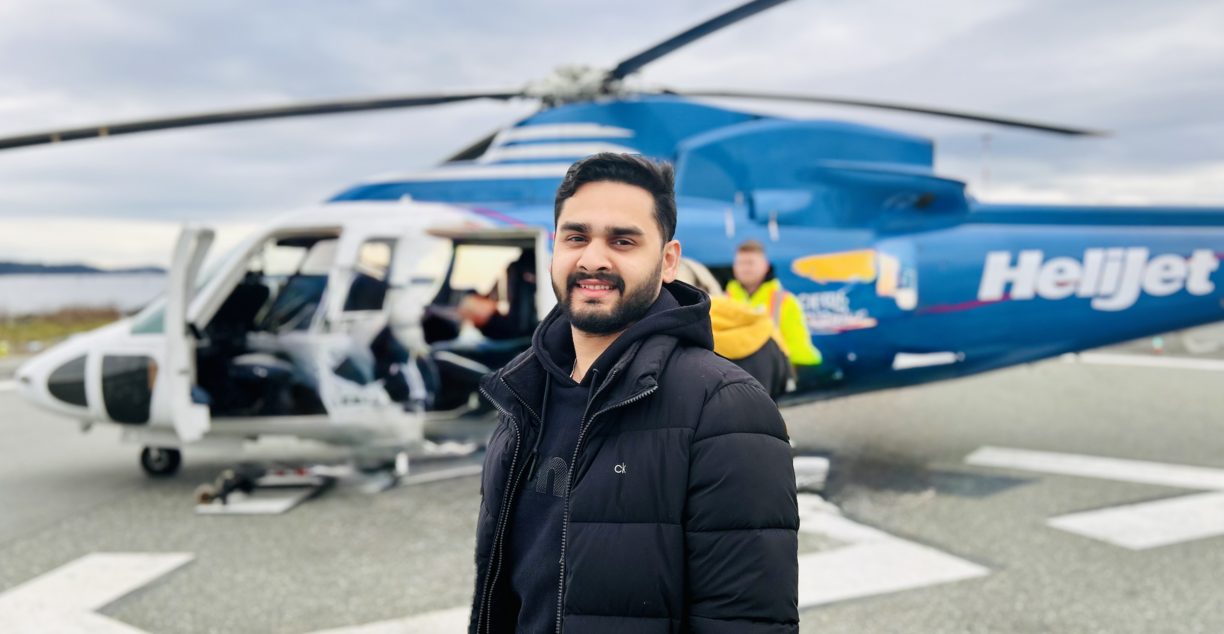Saurya Mishra standing outside in front of a Heli-Jet helicopter and looking at the camera.