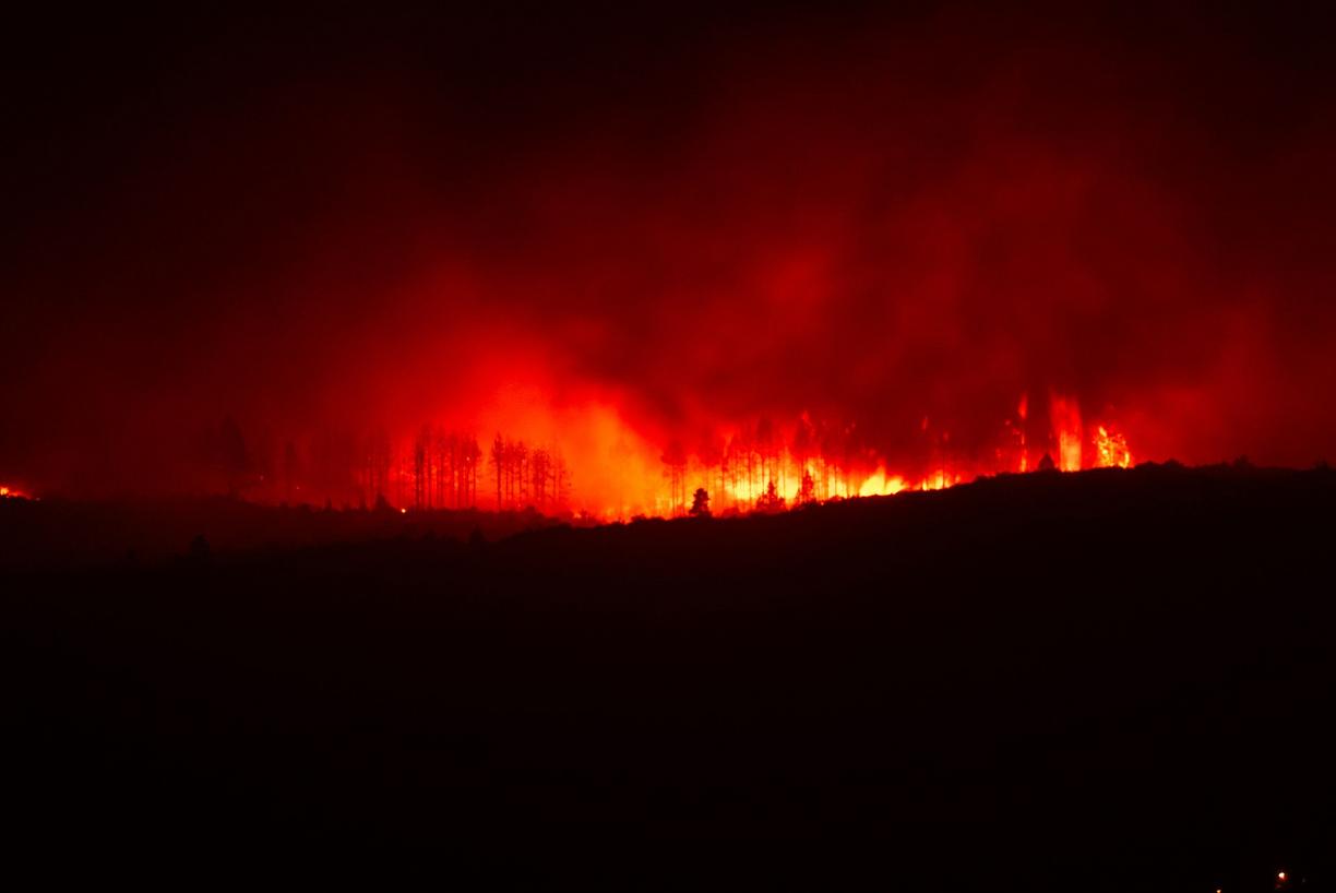 A wildfire burns over a ridge at night