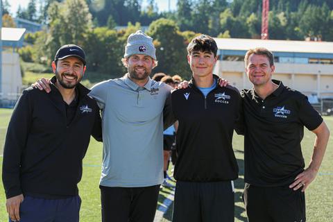 Four men smile on the field at soccer practice