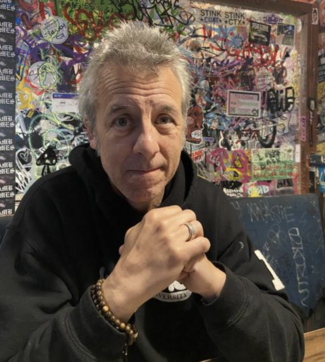 Justin McGrail in a black hoodie with his hands folded in front of him, smiling at the camera.