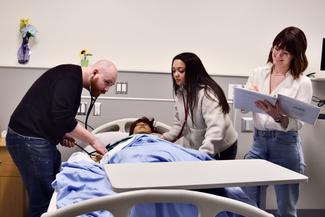 A male nursing student and two female nursing students training in a simulation lab