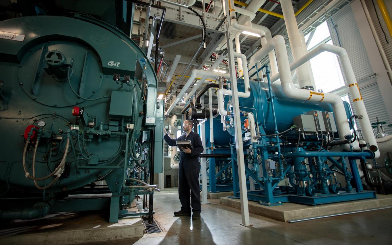 a power engineer inspects large tanks in a big machine room with sunlight peeking through the window