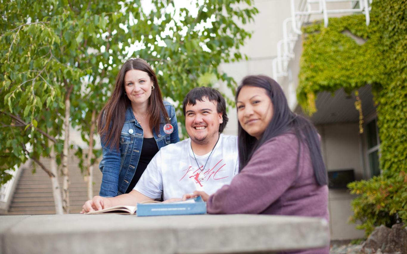 Three students chat around a table outside