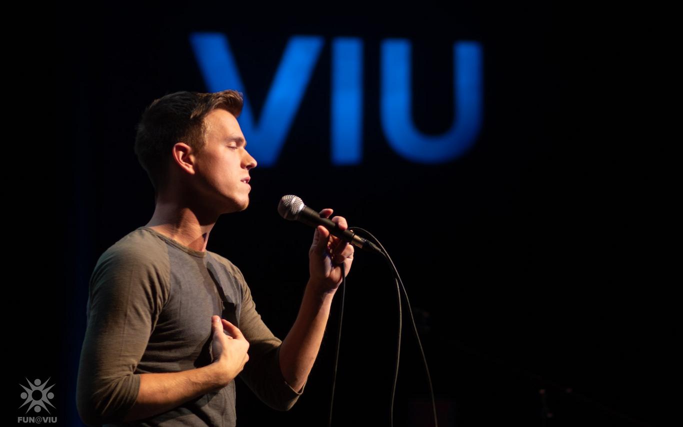 A student sings into a microphone with the VIU logo behind him
