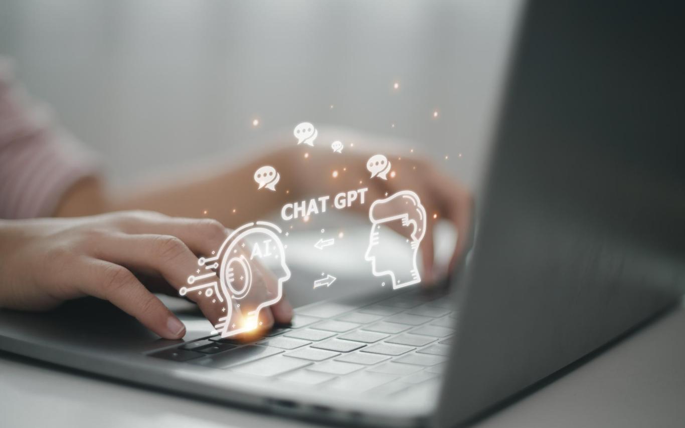 A person typing on a laptop with a graphic of a robot and person with ChatGPT written between them