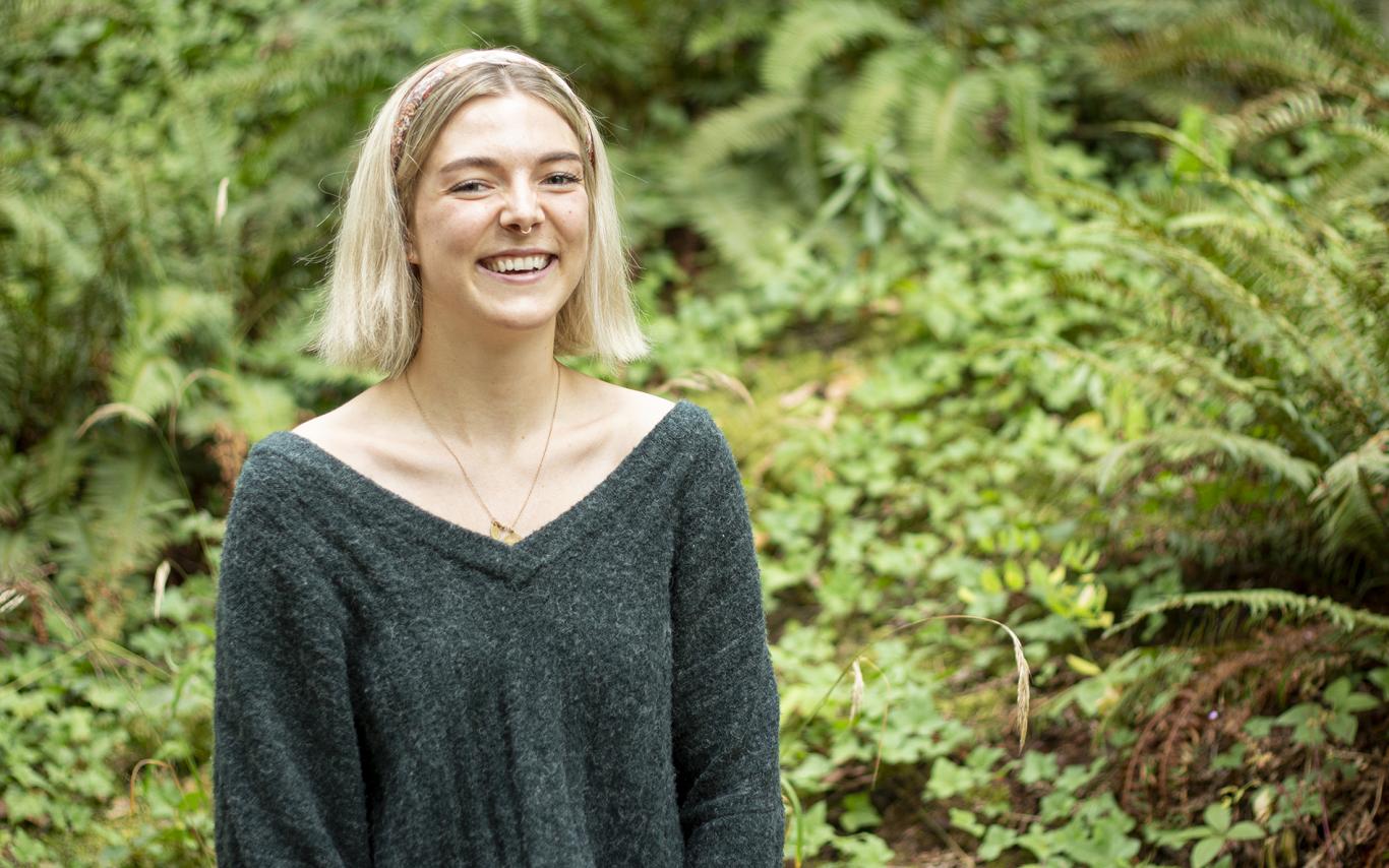 Denman Moody smiles while standing in front of green ferns.