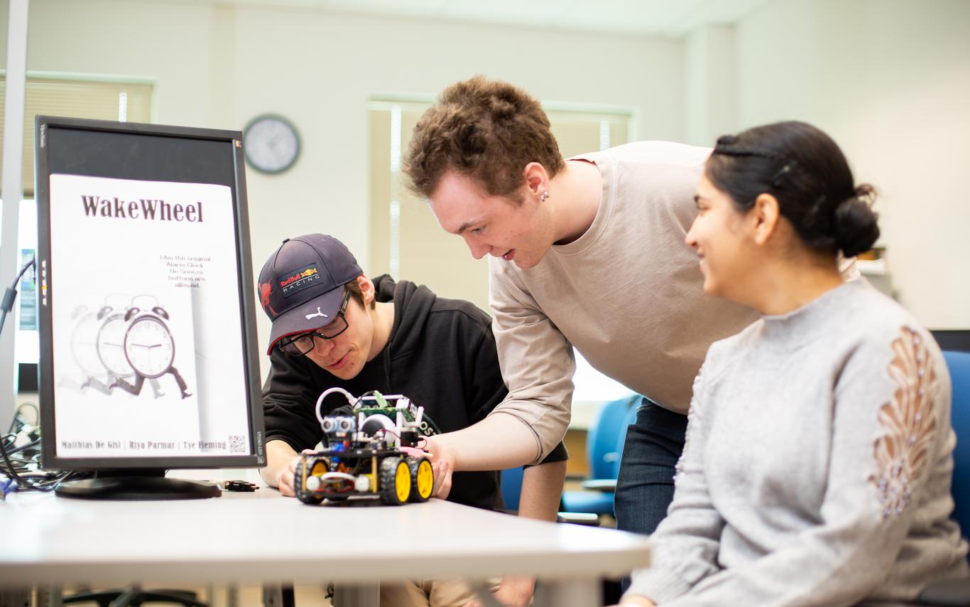 three students look at a robotic car on a table