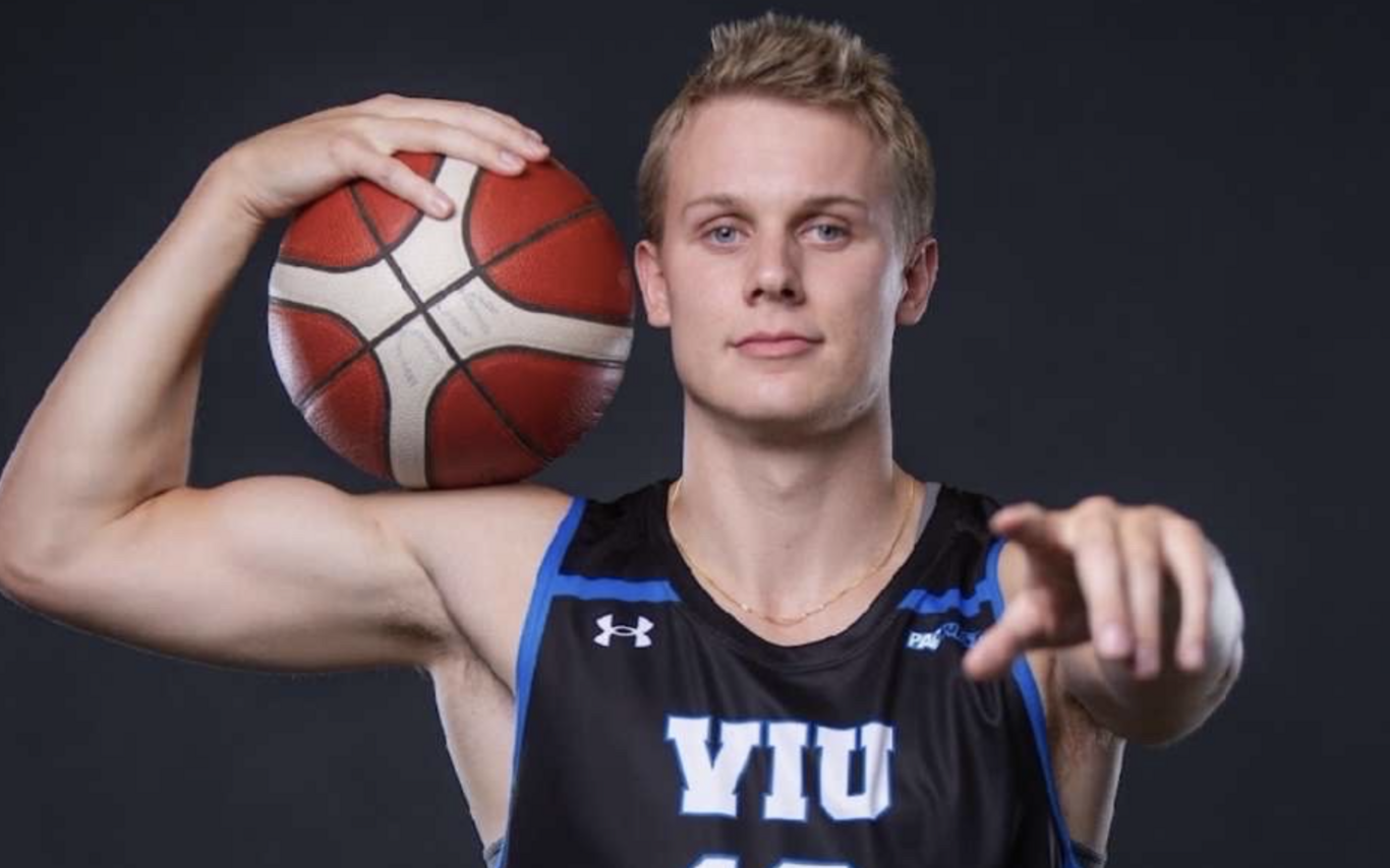 Kai Leighton in a Mariners jersey holding a basketball and pointing at the camera.