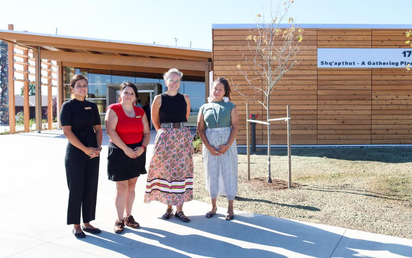 Four people stand in front of Shq'apthut: A Gathering Place