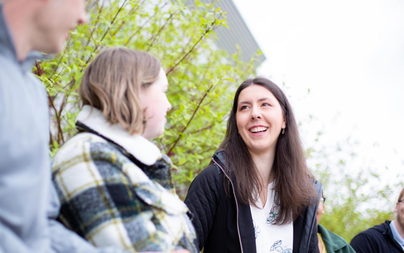 A young woman with long dark hair laghing with friends.