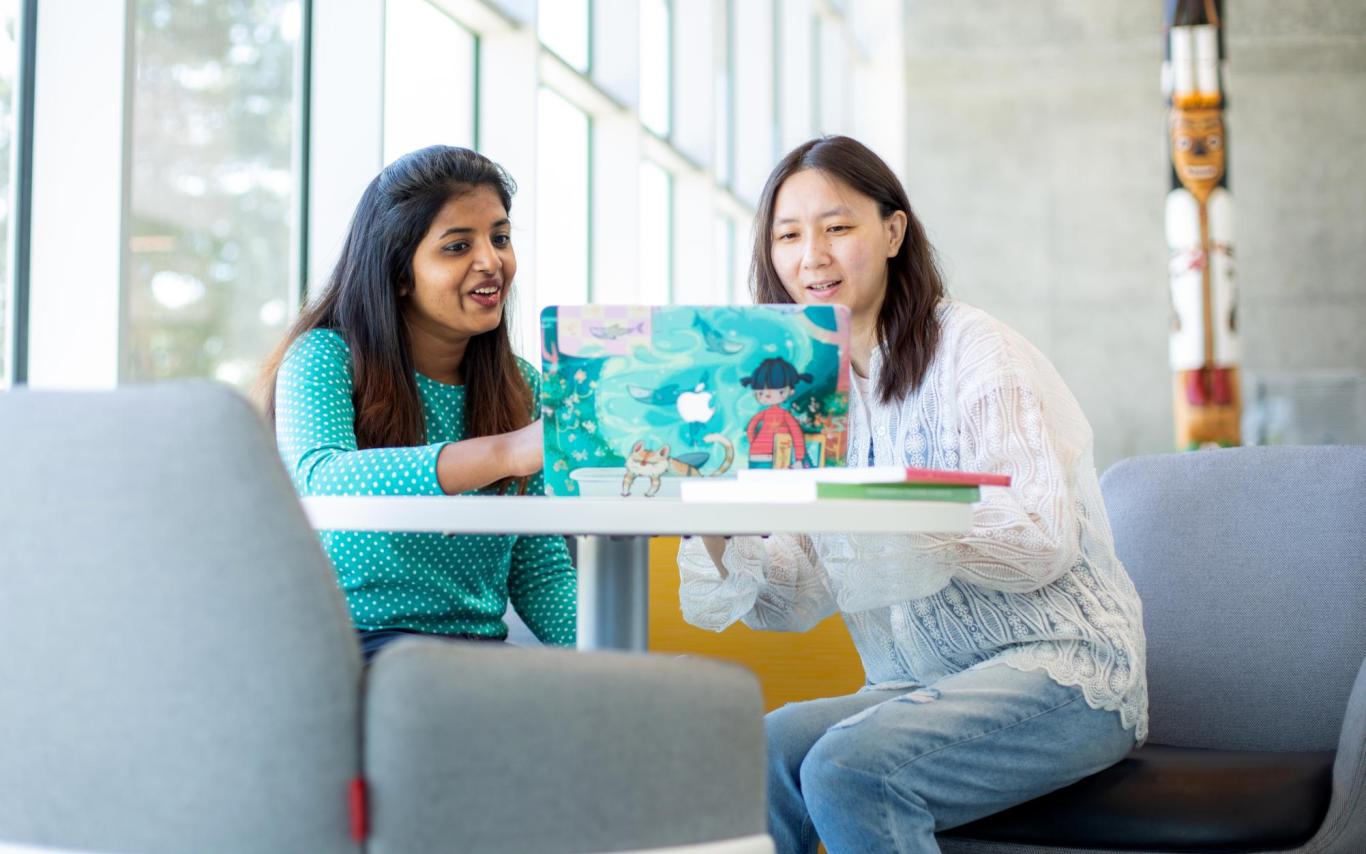 Two women look at a laptop screen together