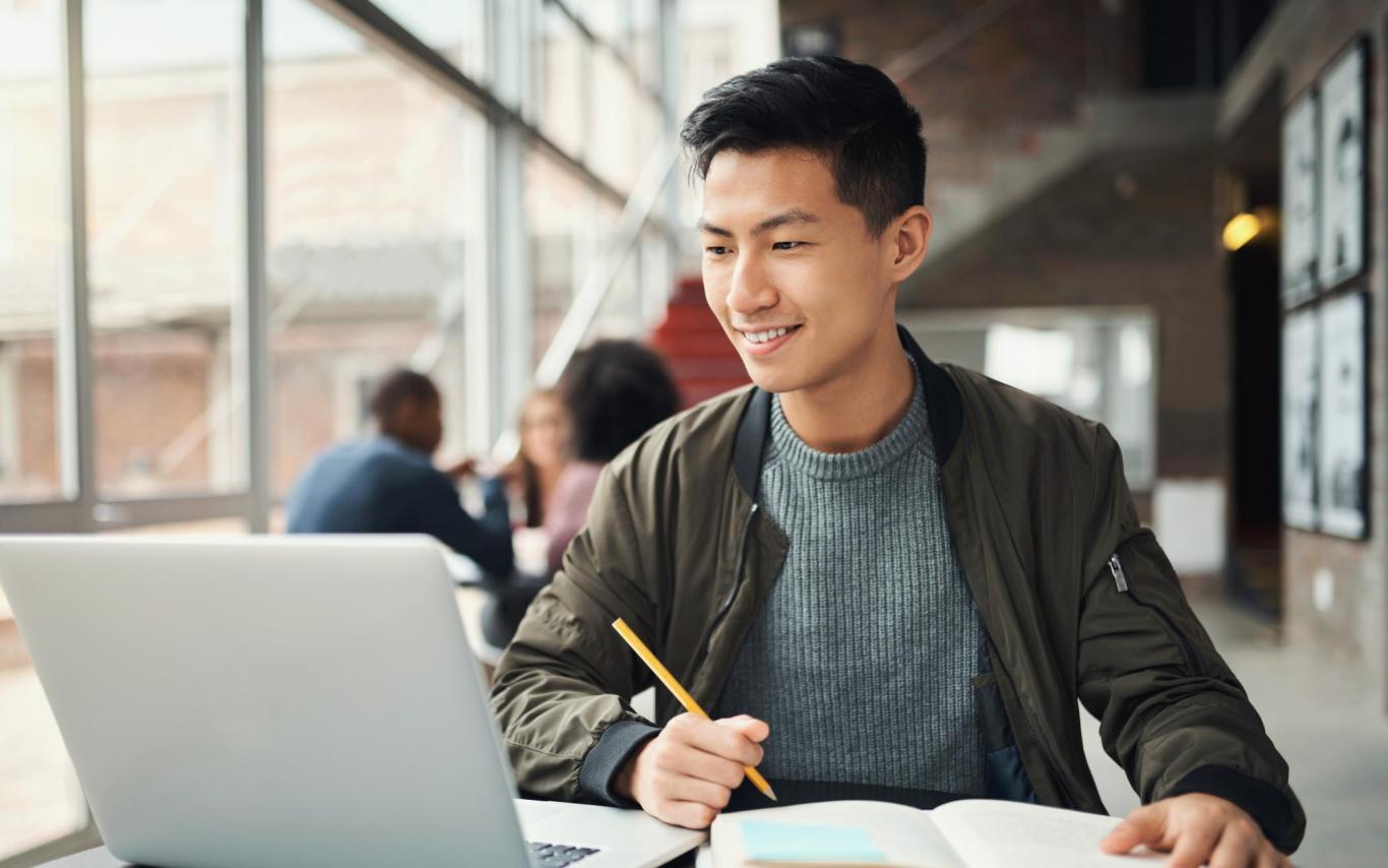Student looks at a laptop screen and takes notes