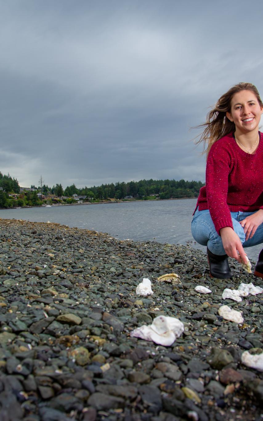 Woman crouches on the beach with shellfish in the foreground