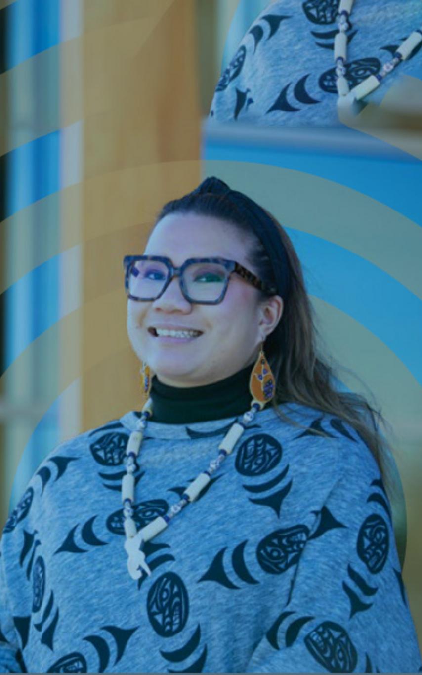 A smiling young woman wearing  Indigenous-themed top and jewelry