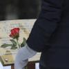 A person holding a rose stands in front of the Jardin des Quartorze garden memorial.